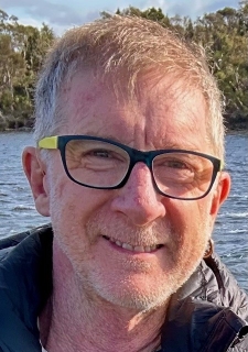 a man with light hair, wearing glasses, smiling. Headshot.