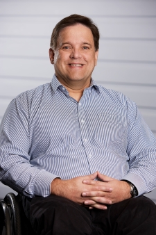 A man, smiling, well dressed in business attire, sitting in a wheelchair