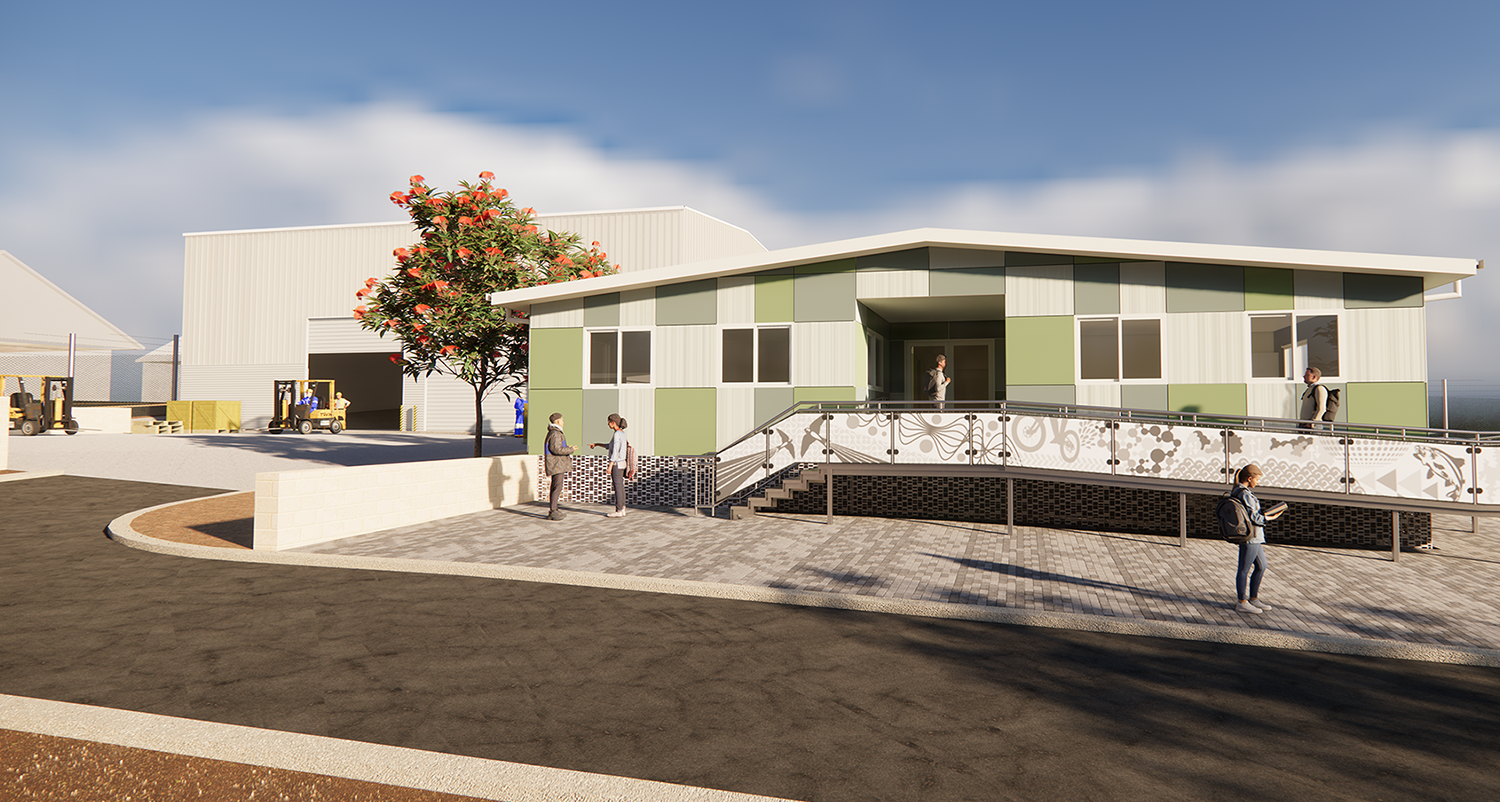 A modern green‑and‑white building with an accessibility ramp in front, with people walking nearby and industrial sheds and forklifts in the background on a sunny day.