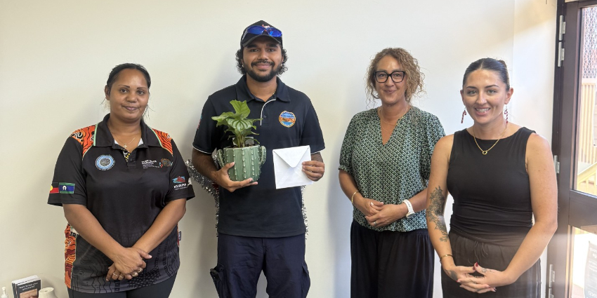 Four people standing and smiling. One holds a gift card and pot plant.