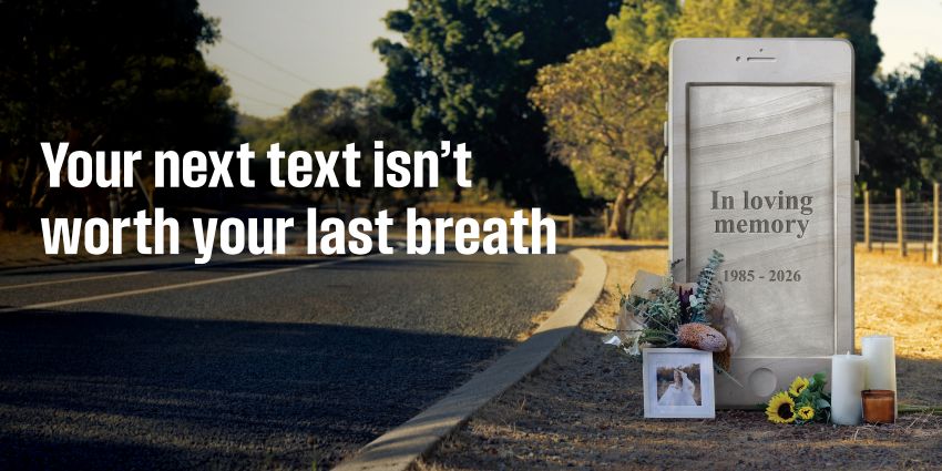 A headstone in the shape of a phone on the side of a road. A woman's belongings are stacked at the base of it.