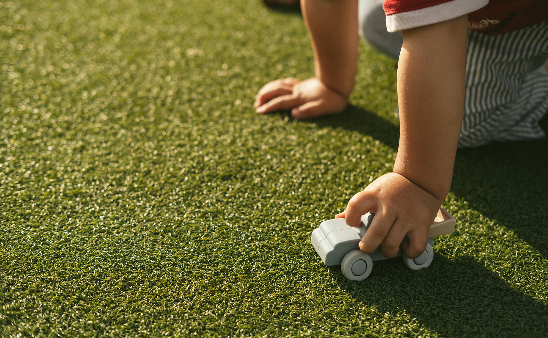 a child's hand holding a toy car on the grass
