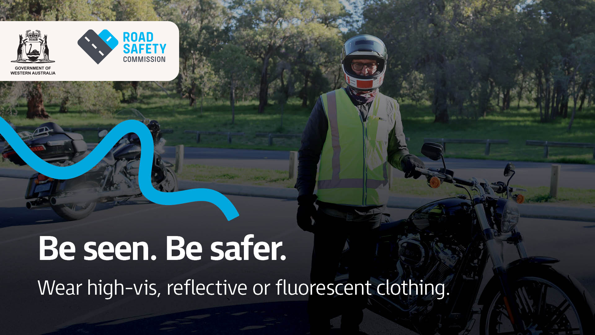 A motorcyclist wearing a helmet and high vis vest standing next to a motorcycle