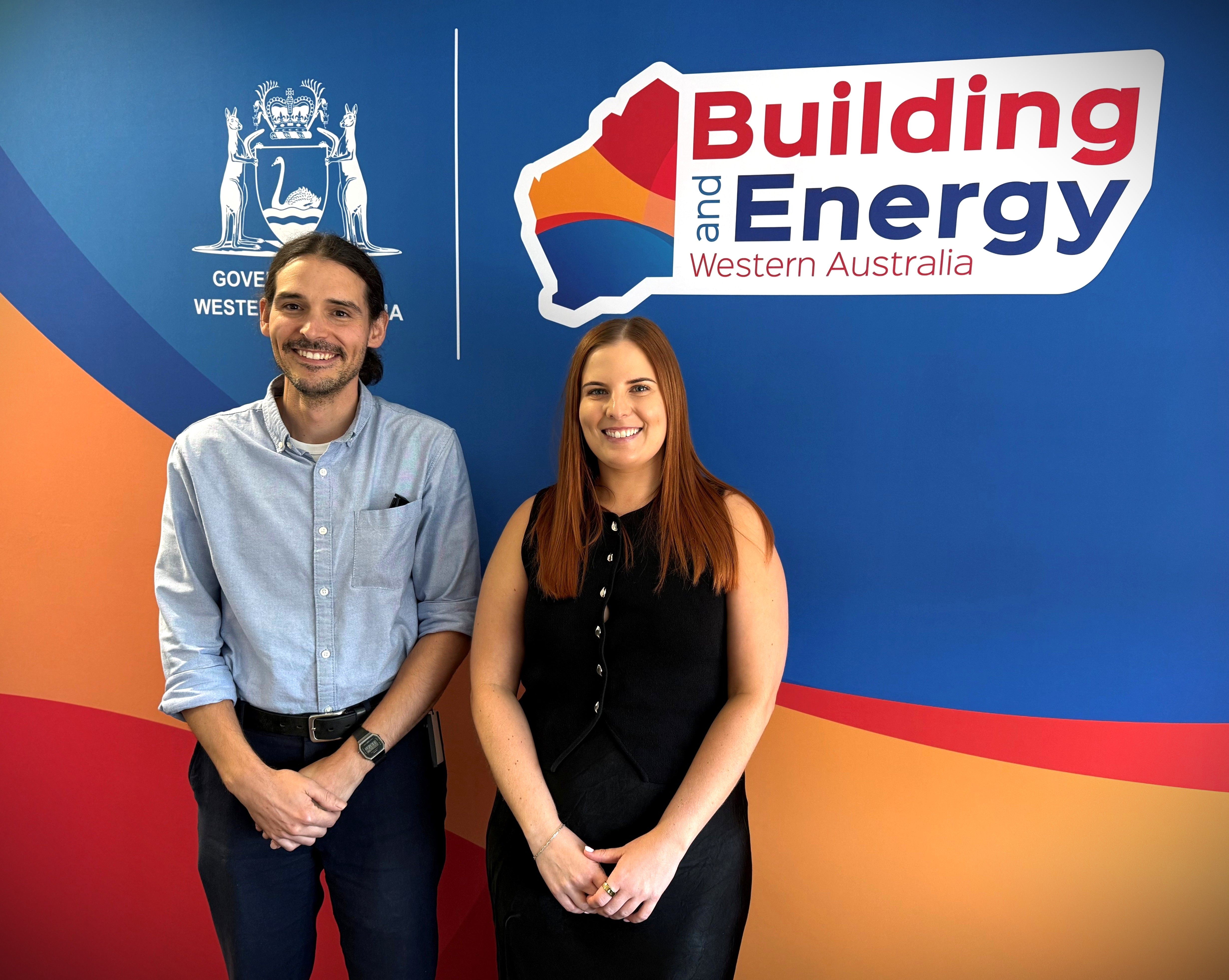 A man and woman stand in front of a Building and Energy logo