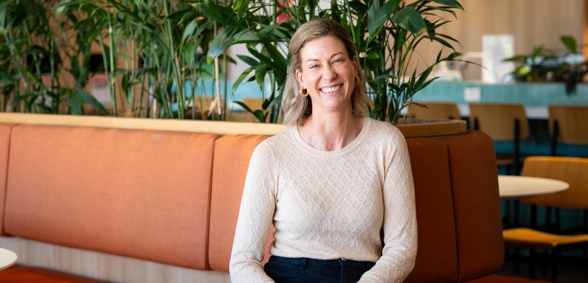 A professionally dressed woman in an indoor setting, smiling
