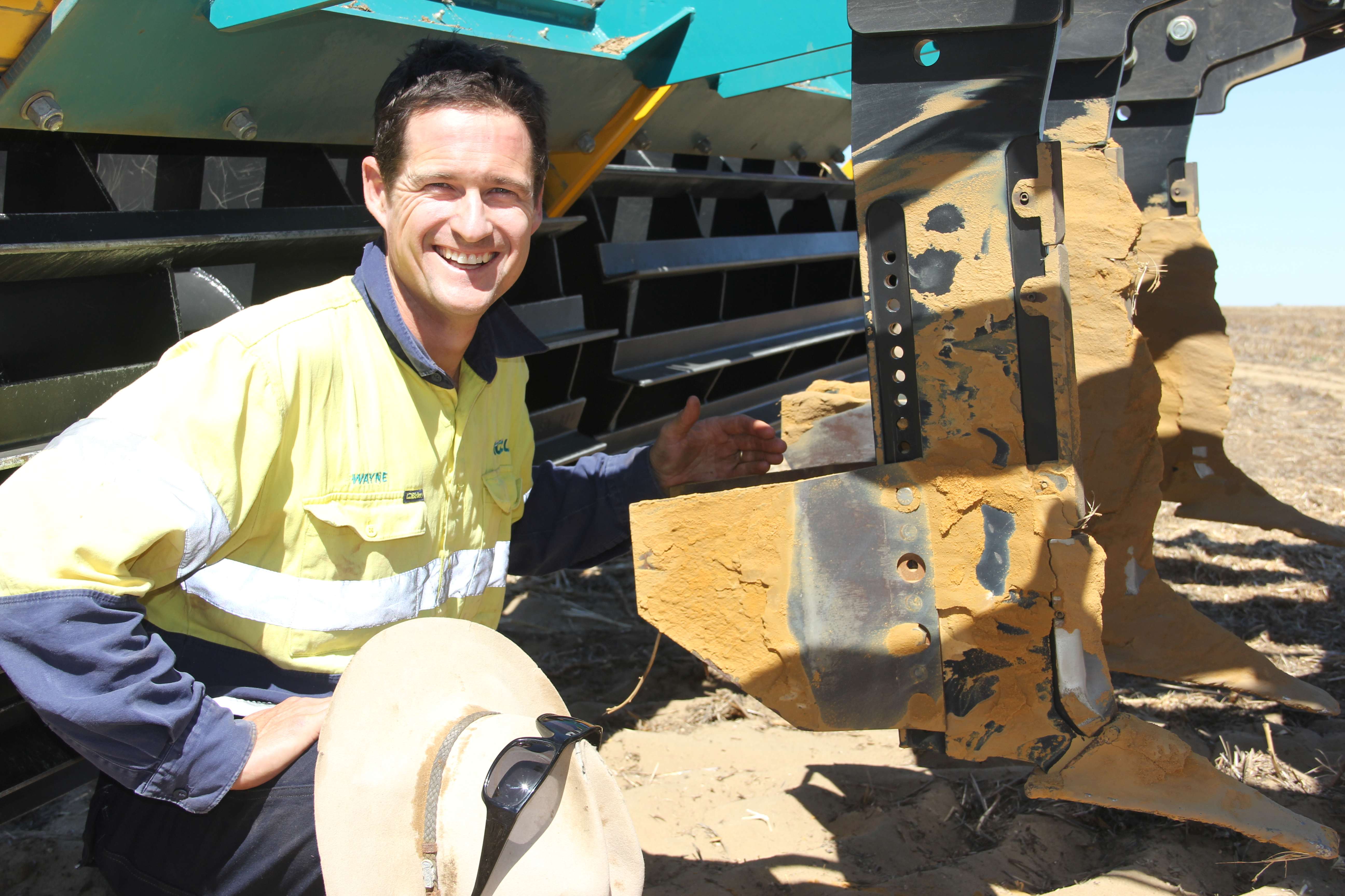 A man crouching next to tines on a seeder.