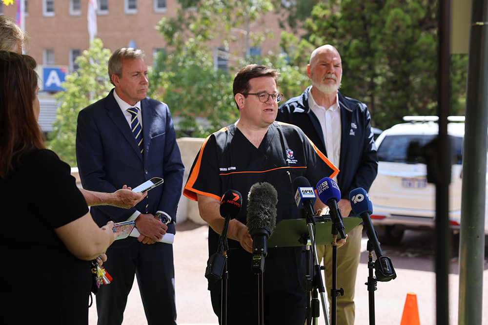 Professor Dieter speaks at a road safety press conference, with Minister Whitby and Commissioner Warner flanking behind him.