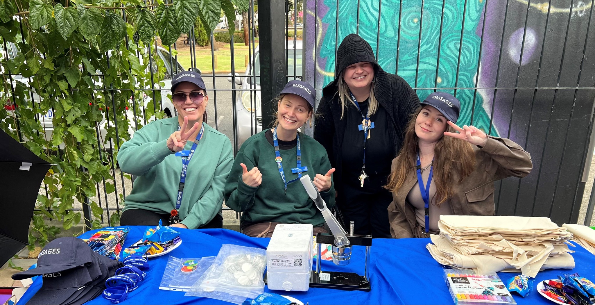 four young women, smiling, wearing lanyards, sitting at a table set up to provide information