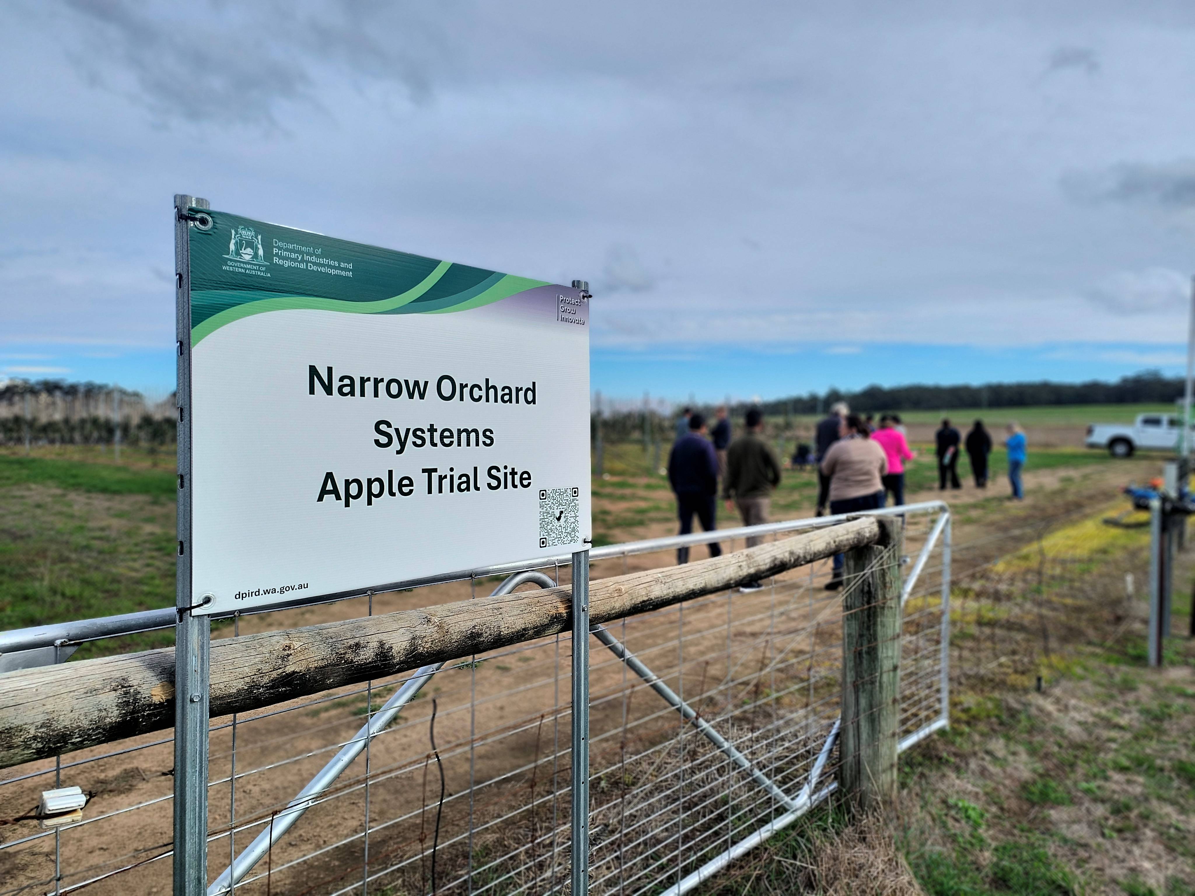 A sign in a paddock with people in the distance.