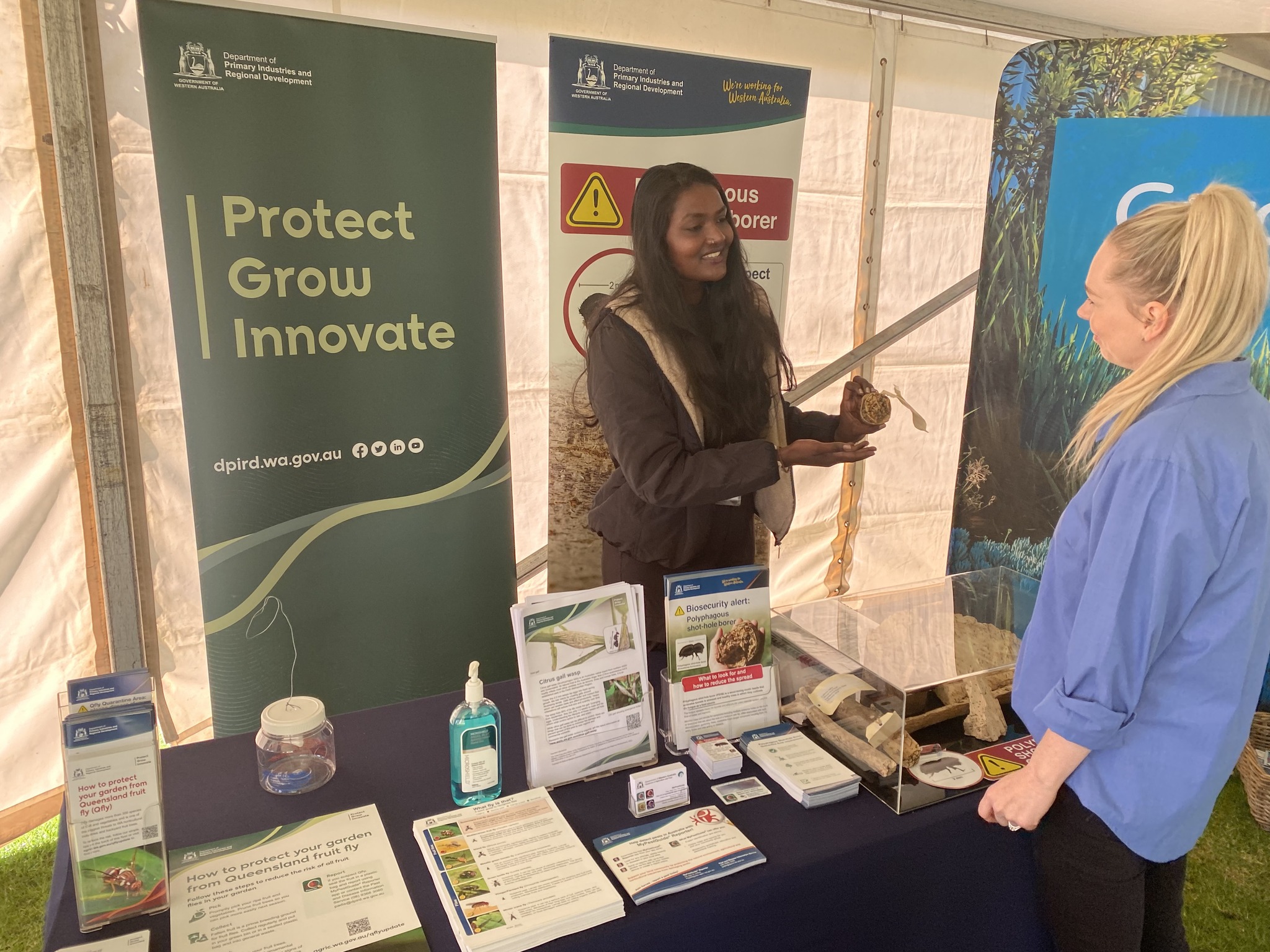 A woman showing another woman a piece of wood in an information display with banners behind.