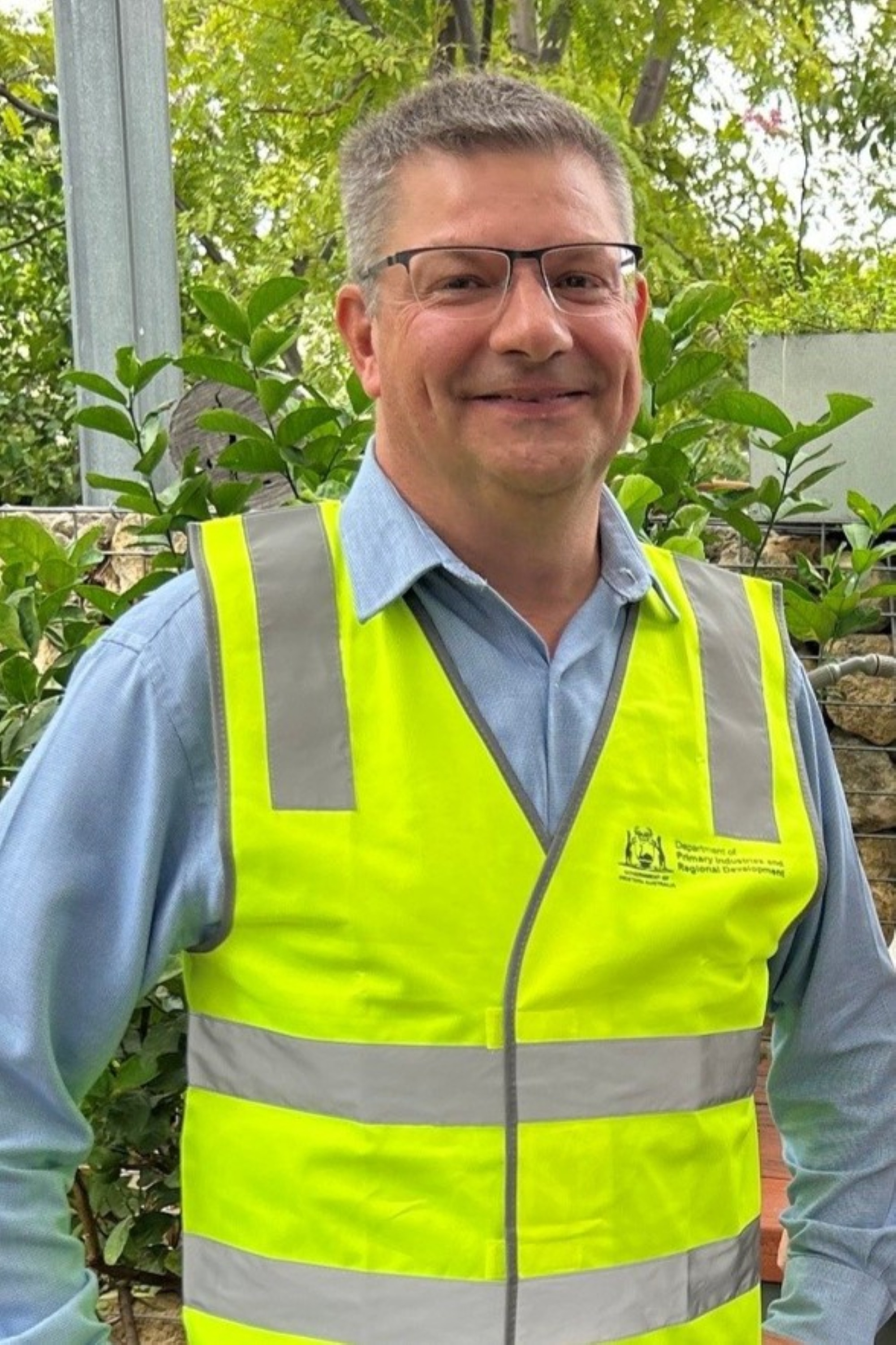 A man wearing a yellow fluro tabbard standing in front of a tree.