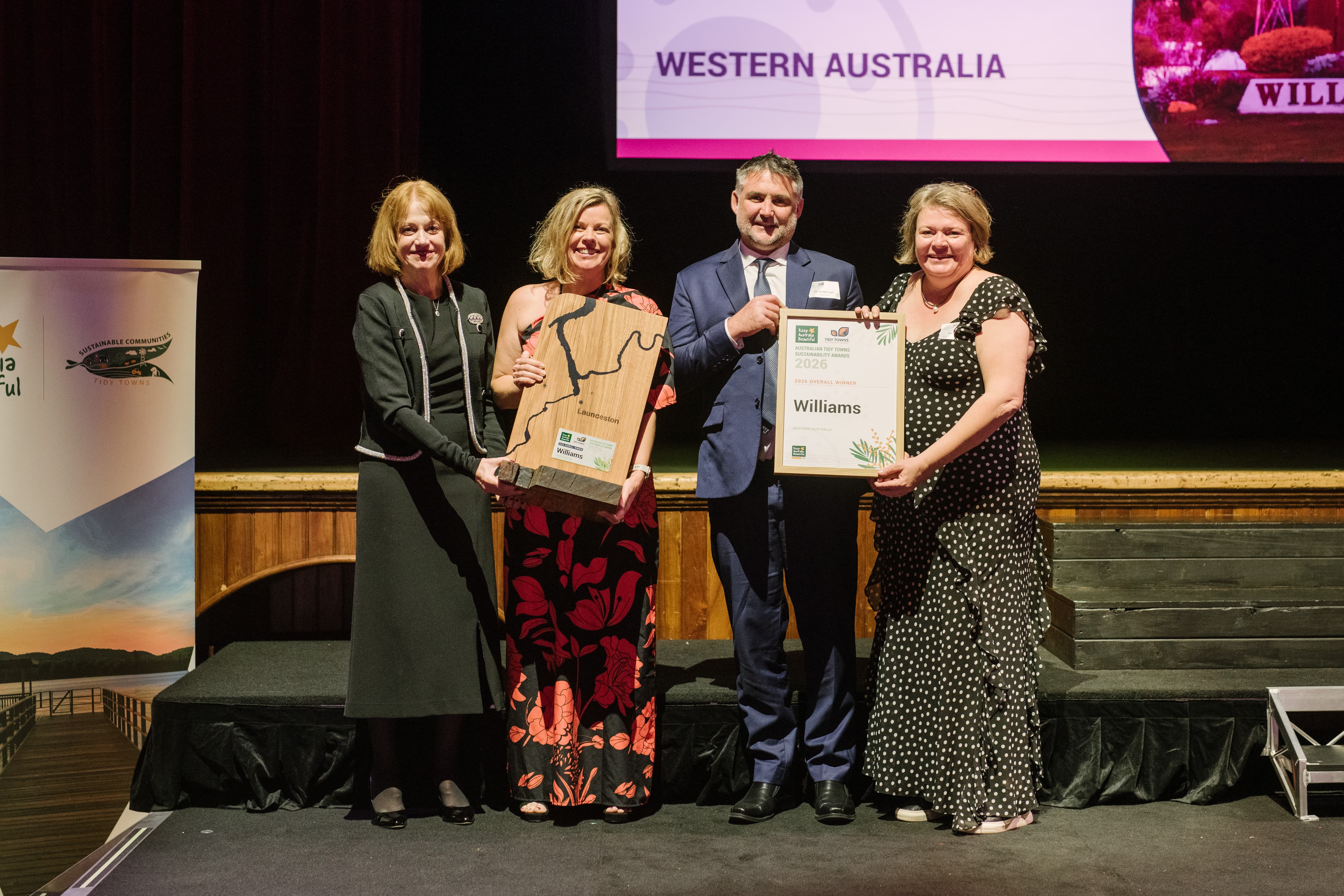 Four people holding an award and certificate on a stage at an awards event.