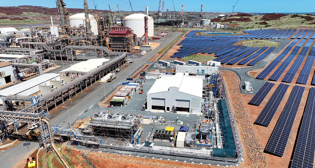 Aerial view of an industrial site with storage tanks, processing structures, and nearby solar panels. 