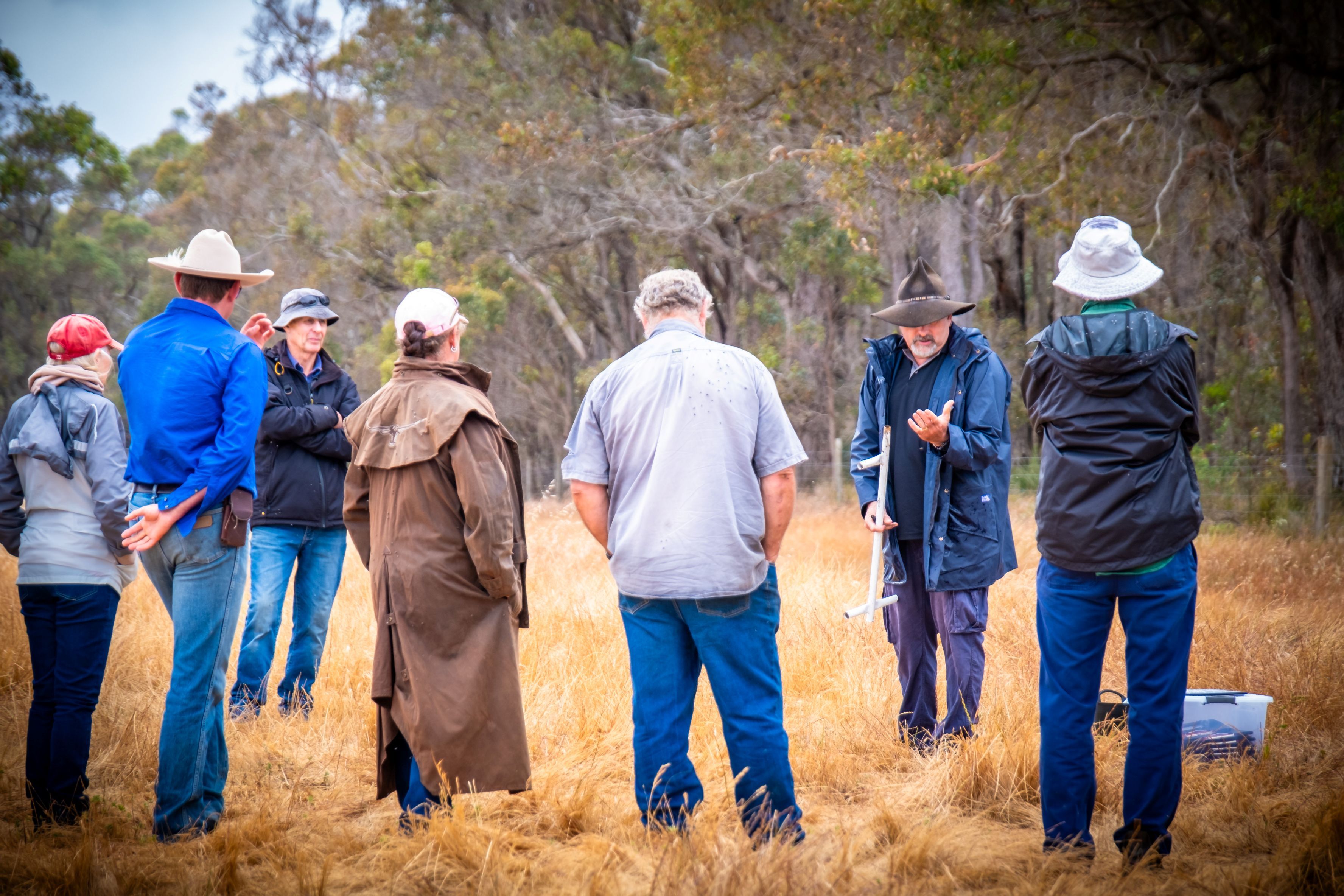 A man demonstrating soil sampling to a group in a dry paddock.