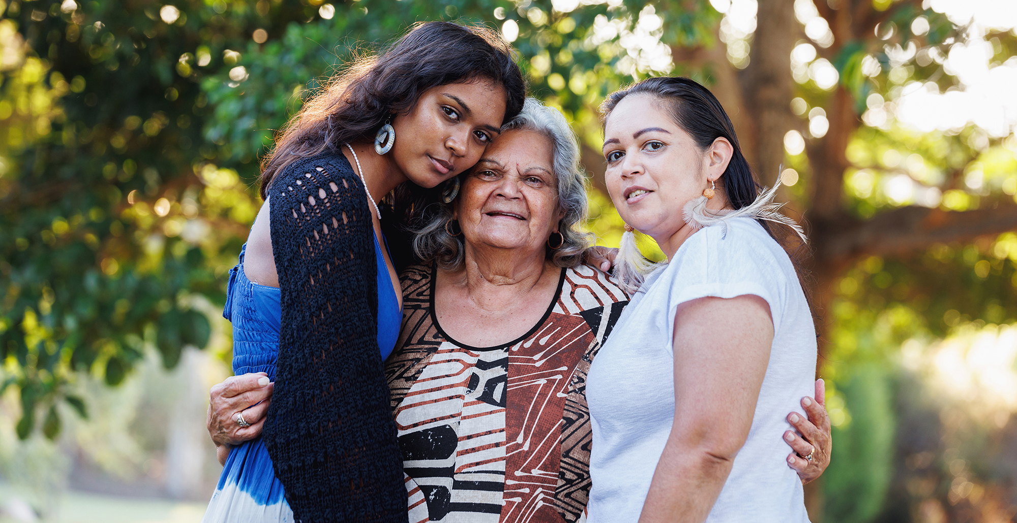 three women, one old and two young, hugging, in an outdoor setting