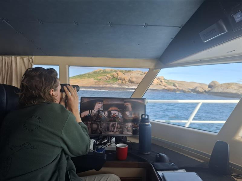 A person looking through binoculars at an island from a vessel.