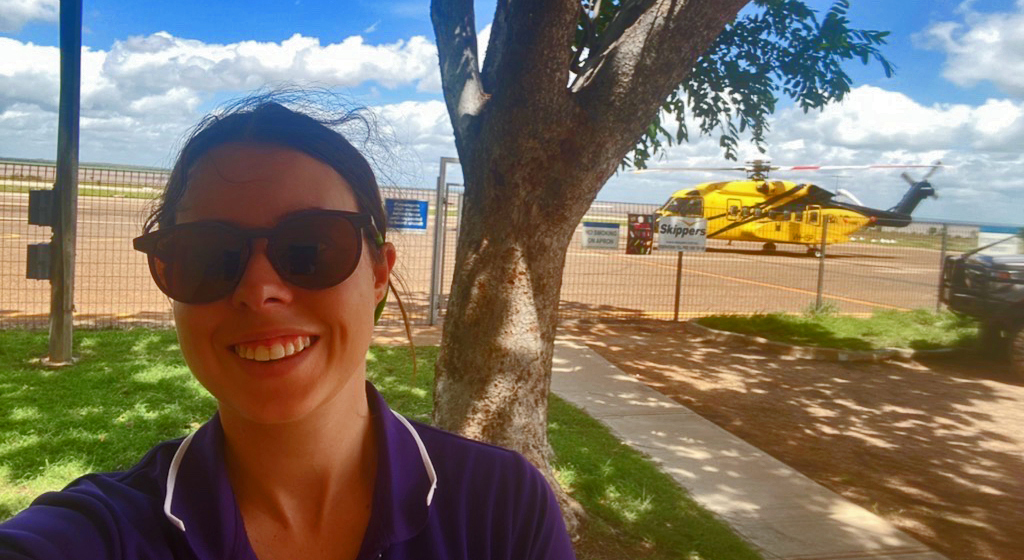 A young woman wearing glasses with a helicopter in the background that she's about to board
