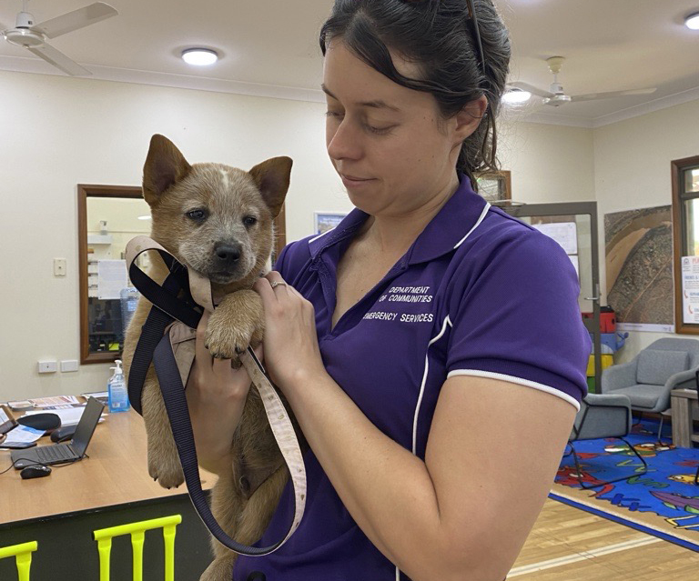 A young women waring an emergency services polo shirt and holding a small dog affectionately in an indoor setting