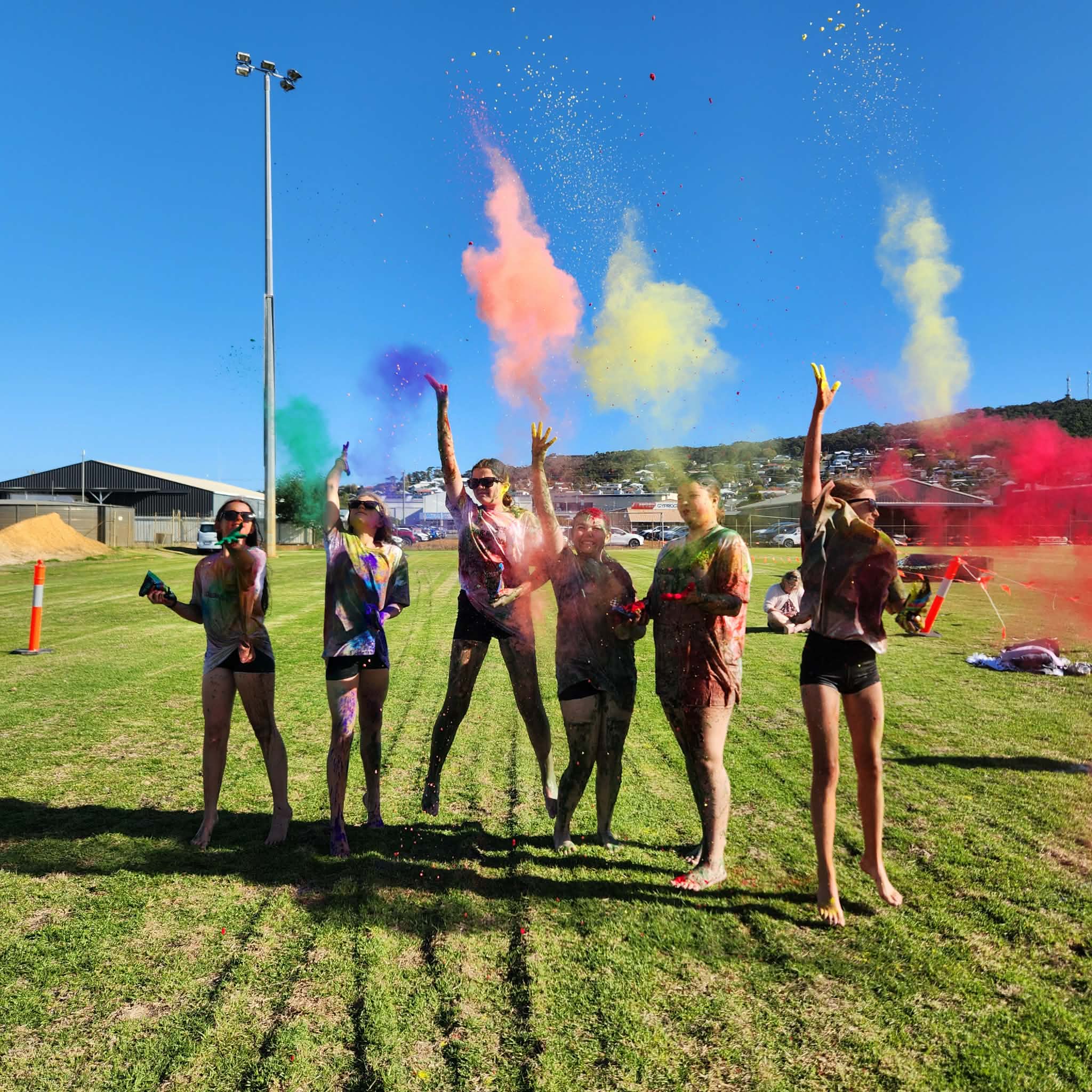 six young adults on a grass oval having fun at the colour run event