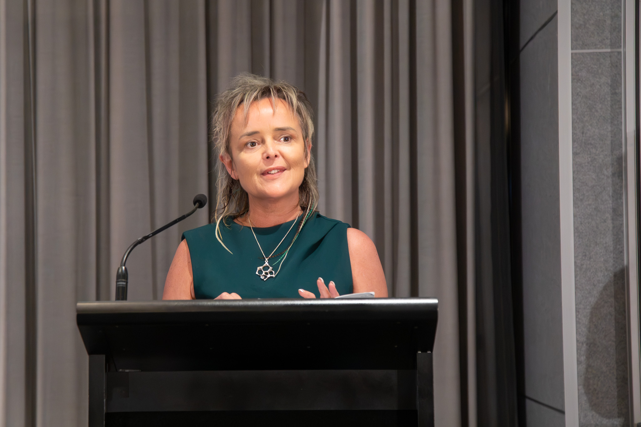 Caroline Speirs speaking at a lectern with a microphone in front of grey curtains at the Child Protection Excellence Awards.