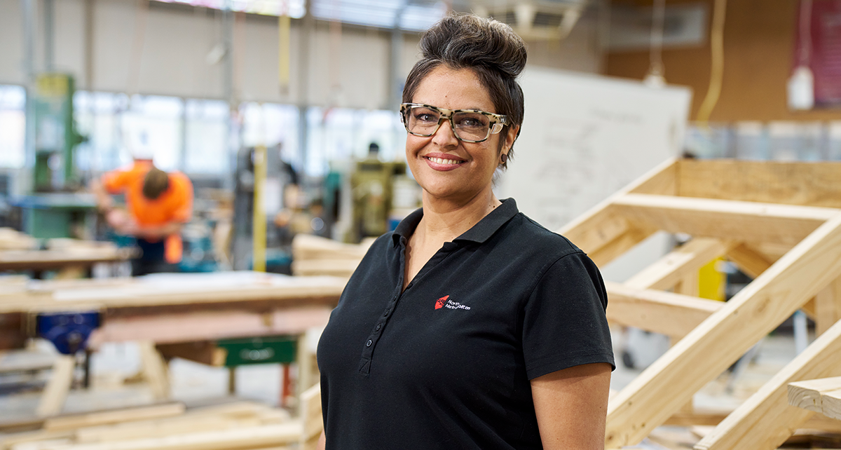 TAFE lecturer standing in a carpentry workshop beside a timber frame.