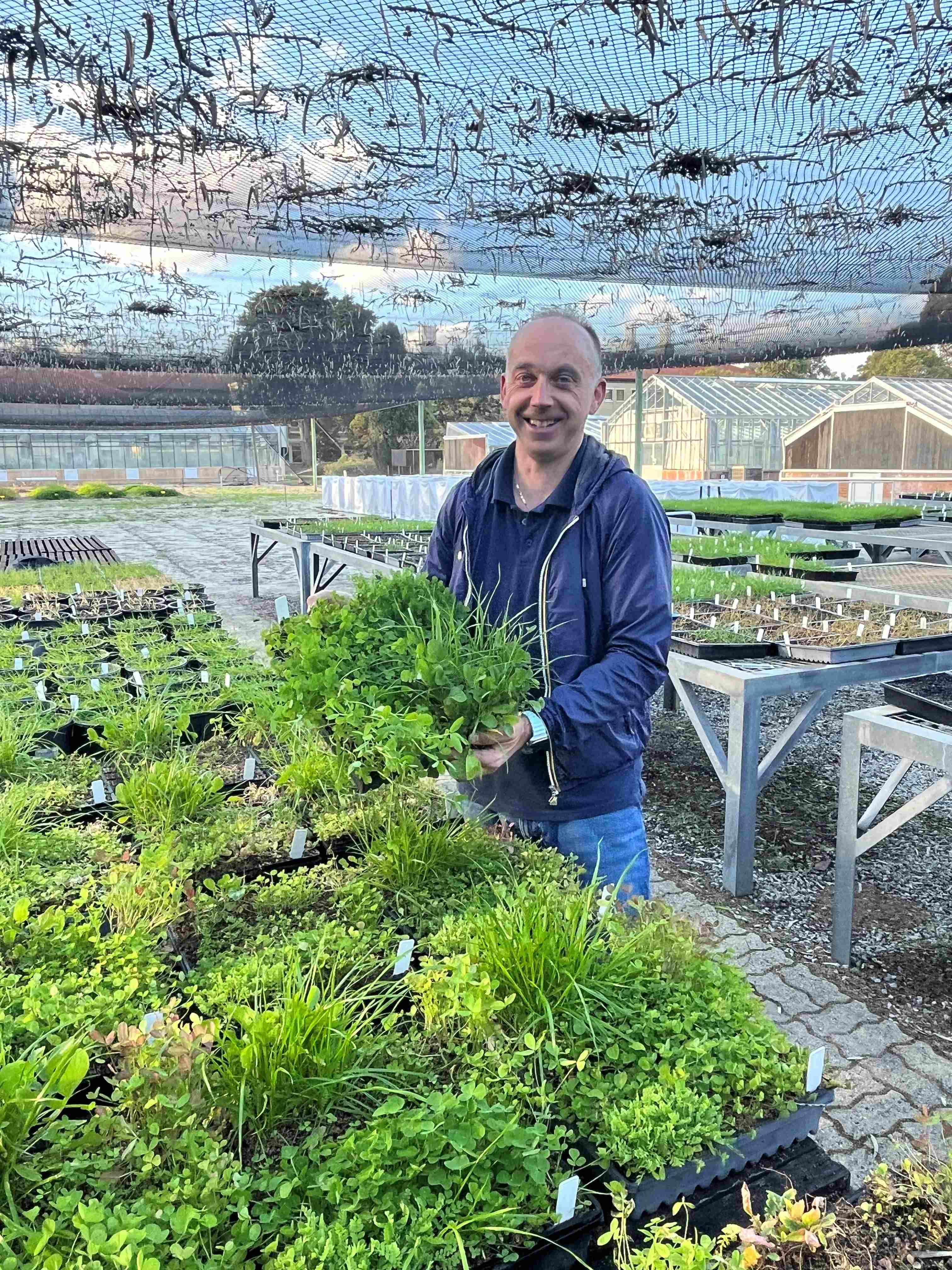 A man standing in a greenhouse with tables of potted plants.