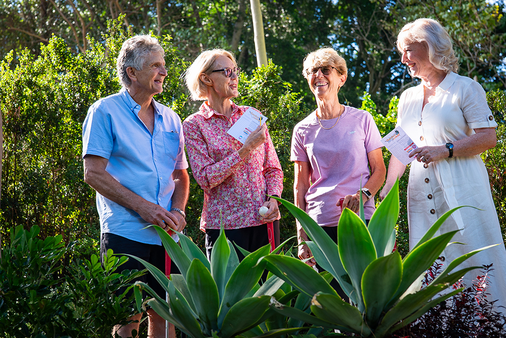 A group of four older people, smiling, well dressed, in a garden surrounding