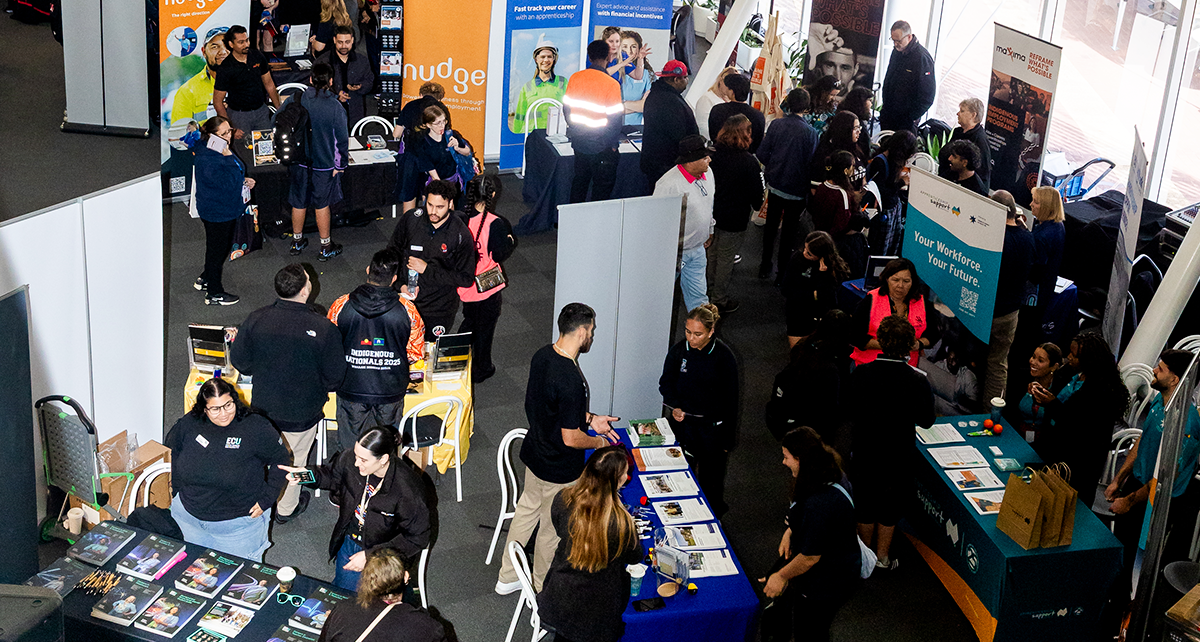 Busy Deadly Jobs Expo with attendees visiting exhibition booths, speaking with representatives, and browsing training and employment information.
