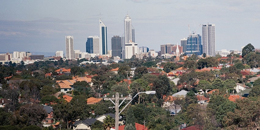 Foreground of house roofs and trees and a background of the city skyline.