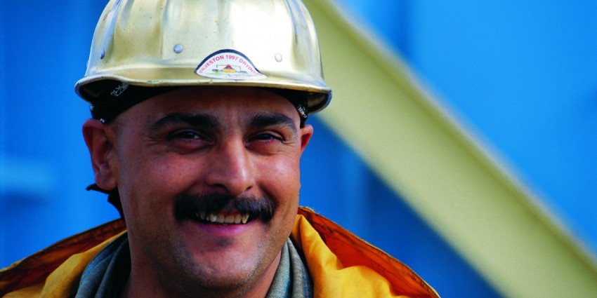 Construction worker with a mustache wearing a hard hat.