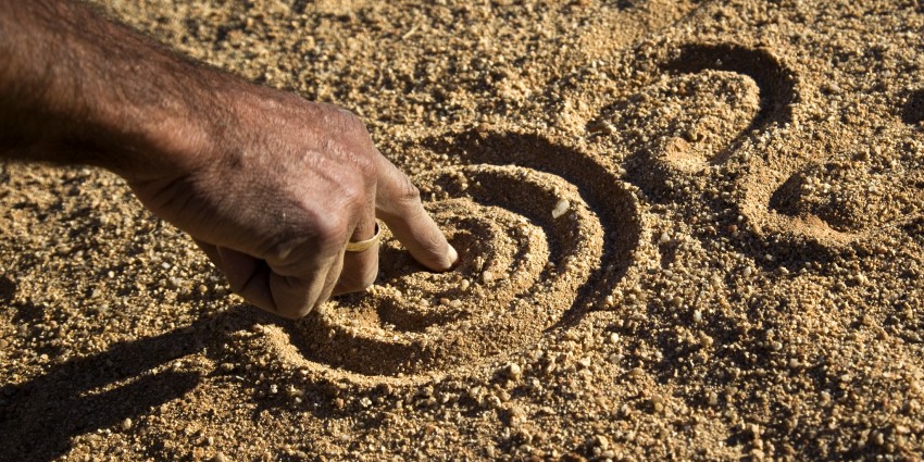 A man's arm, using his index finger to draw shapes in the sand