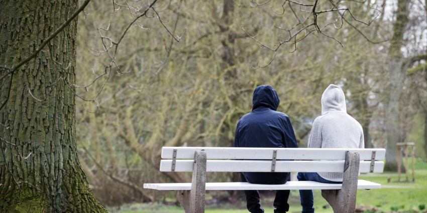 Two people in hoodies sitting on a park bench