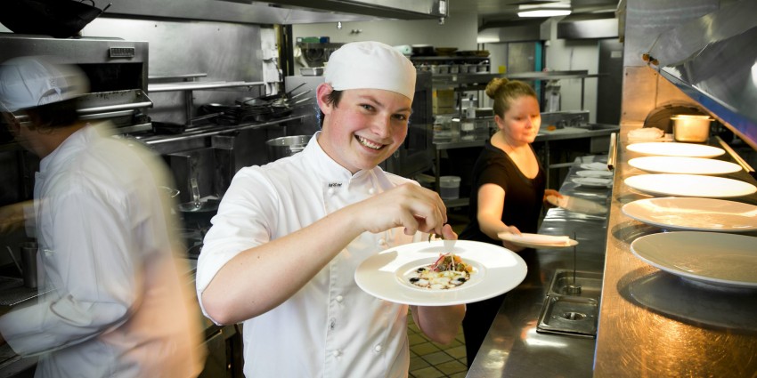 Young apprentice garnishing a dish in the kitchen