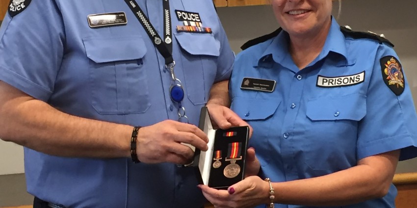 A male police officer in uniform stands with a female prison officer in uniform presenting her with a medal