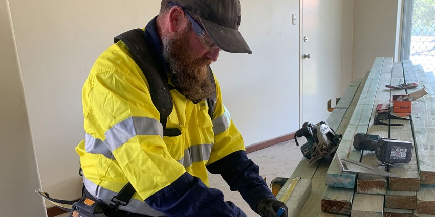Worker in a high visibility vest using a ruler and pencil to mark measurements on timber.