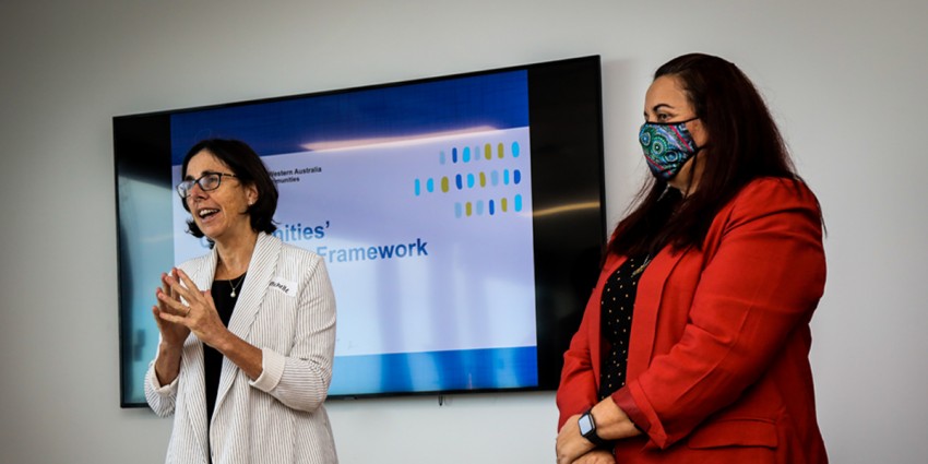 Communities’ Director General Michelle Andrews and Western Australian Council of Social Service Chief Executive Louise Giolitto standing in front of a large TV screen mounted on a wall at the launch of the Communities Partnership Framework.