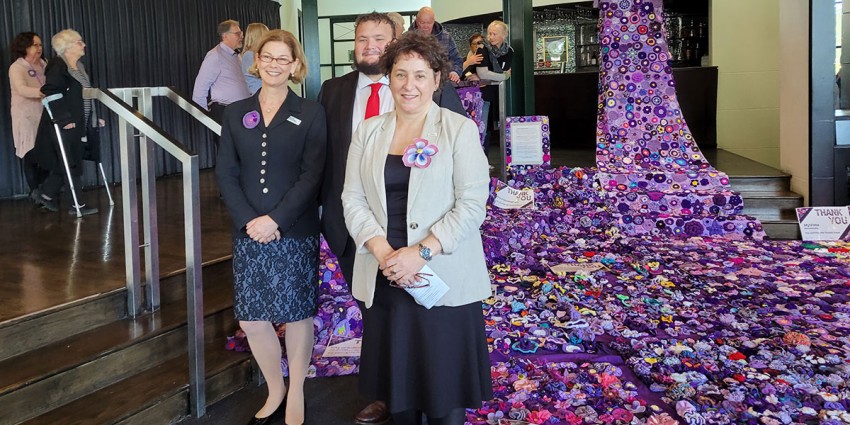 Hon Meredith Hammat, Hon Kyle McGinn and Kathy Blitz-Cokis standing in front of the Purple Road artwork.