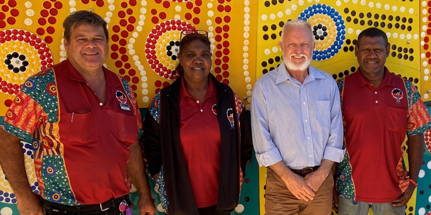 Staff from the Department of Communities and Yura Yungi Medical Service Aboriginal Corporation standing together in front of Aboriginal artwork.