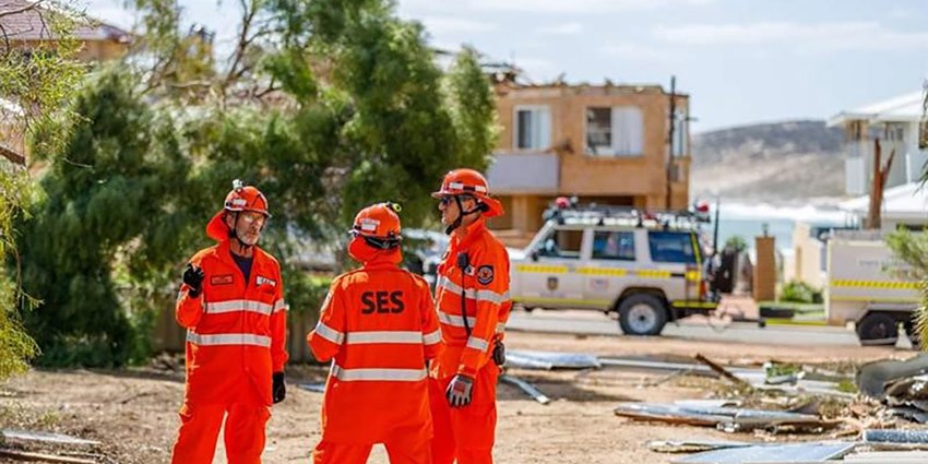 Three State Emergency Service responders standing in front of a cyclone aftermath