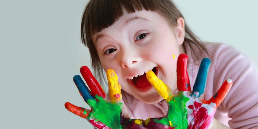 A young girl smiling, with colourful paint on her hands.