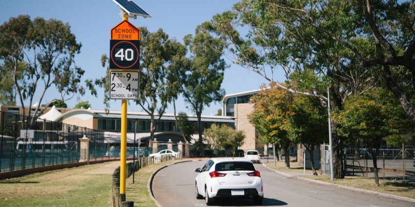 Car driving into school next to school zone speed limit sign