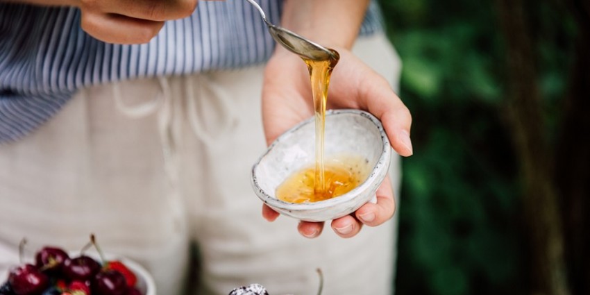 Man holding spoon with honey dripping into a small bowl