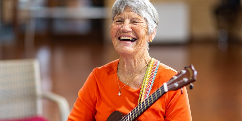 photo of older person - she is smiling and playing a guitar