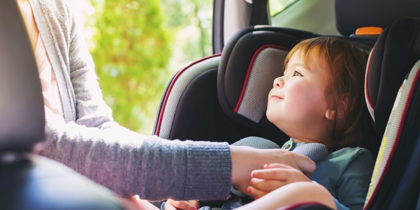 Mum buckling a toddler into a car seat