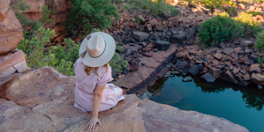 Image of young woman sitting on rock ledge overlooking waterhole in the kimberley 