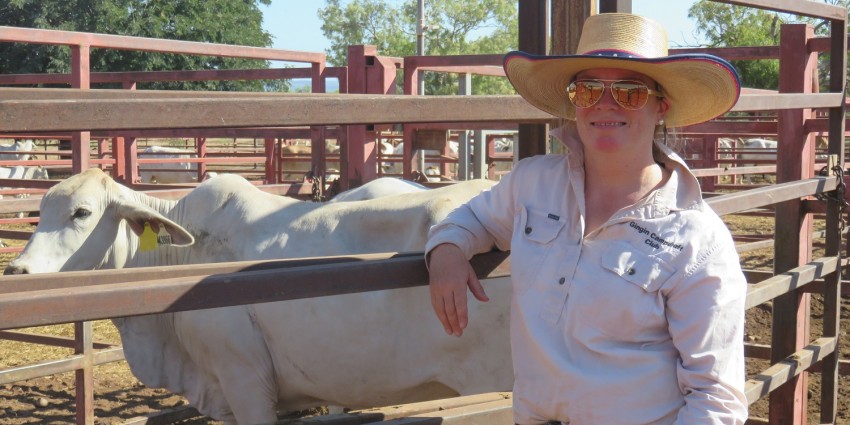 A female cattle handler posing in front of cows in a pen