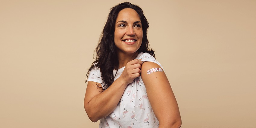 A photo showing a person rolling up their sleeve with a band-aid on their arm.
