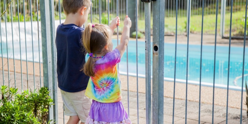 Two young children standing outside of a pool safety barrier.