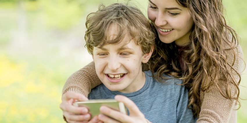 A woman and young boy looking at a mobile phone together, smiling.