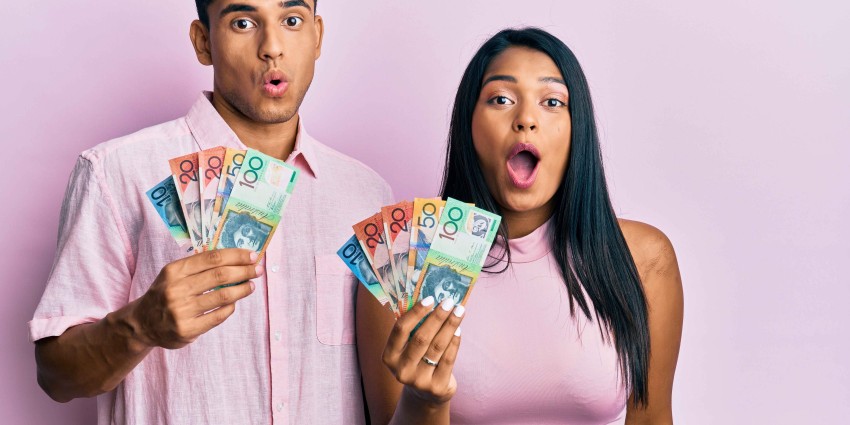 Young couple holding Australian dollars scared and amazed with open mouth for surprise, disbelief face